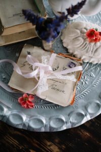 A close-up of vintage handwritten love letters tied with a delicate pink ribbon, styled with small red and purple flowers on a silver tray.