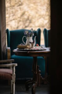 A cozy reading nook at Fairy Oak cottage featuring a plush teal armchair next to a window and a decorated wooden side table.