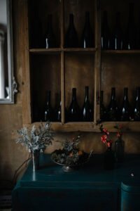 Moody interior view of dark wooden shelves filled with wine bottles above a decorated rustic sideboard.