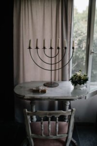 Vertical view of a classic multi-armed candlestick holder standing on a rustic wooden table under soft, muted window light.