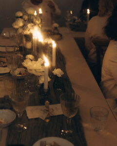 A moody and romantic wedding reception table illuminated by tall white taper candles, decorated with delicate white floral centerpieces in a dimly lit setting at Fairy Oak in Fruška Gora.