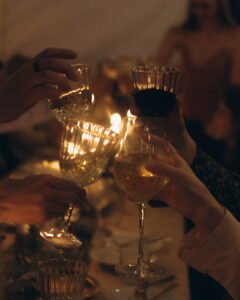 A warm, close-up shot of guests' hands clinking crystal goblets and wine glasses together in a celebratory toast during an evening wedding reception at Fairy Oak.