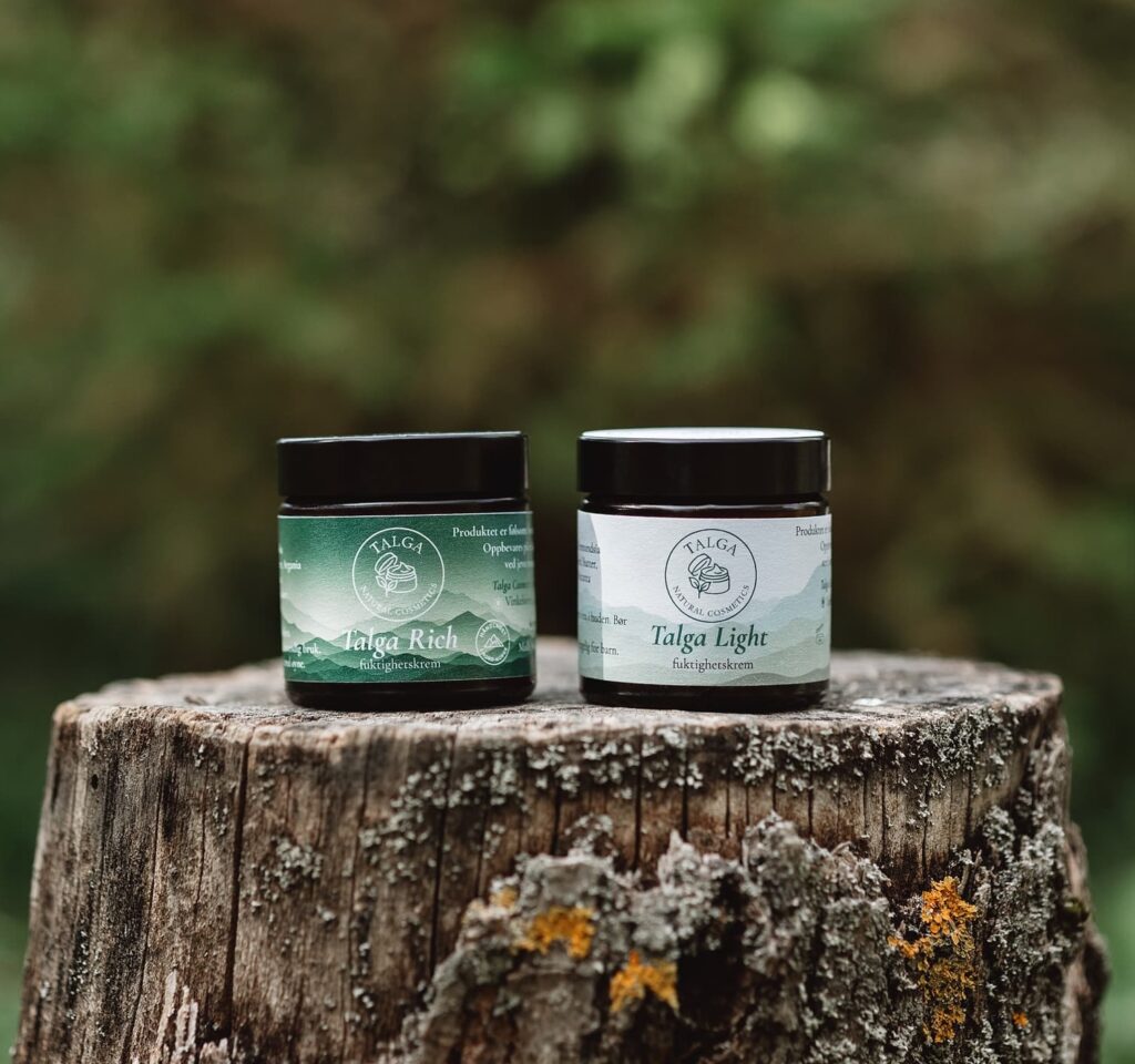 Two dark glass jars of Talga Cosmetics resting on a textured, mossy tree stump against a deeply blurred, lush green forest background during a commercial brand shoot at Fairy Oak.
