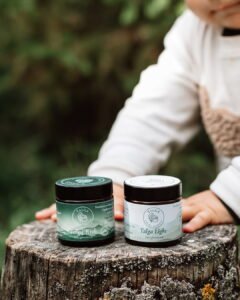 Two dark glass jars of Talga face cream—Talga Rich and Talga Light—over a rustic tree stump during an outdoor lifestyle commercial shoot at Fairy Oak.