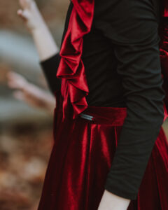 A close-up detail shot of Treger brand children's clothing, focusing on a rich red velvet skirt with a small metallic Treger brand tag and a black long-sleeve top featuring striking red velvet ruffle accents.