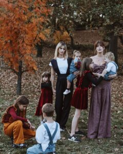 Tregertim founders, Tamara Dragičević and Marija Matić, and children pose together outdoors in a beautiful autumn setting at Fairy Oak. They are modeling Tregertim brand fashion, featuring stylish suspender pants, overalls, and red velvet dresses.